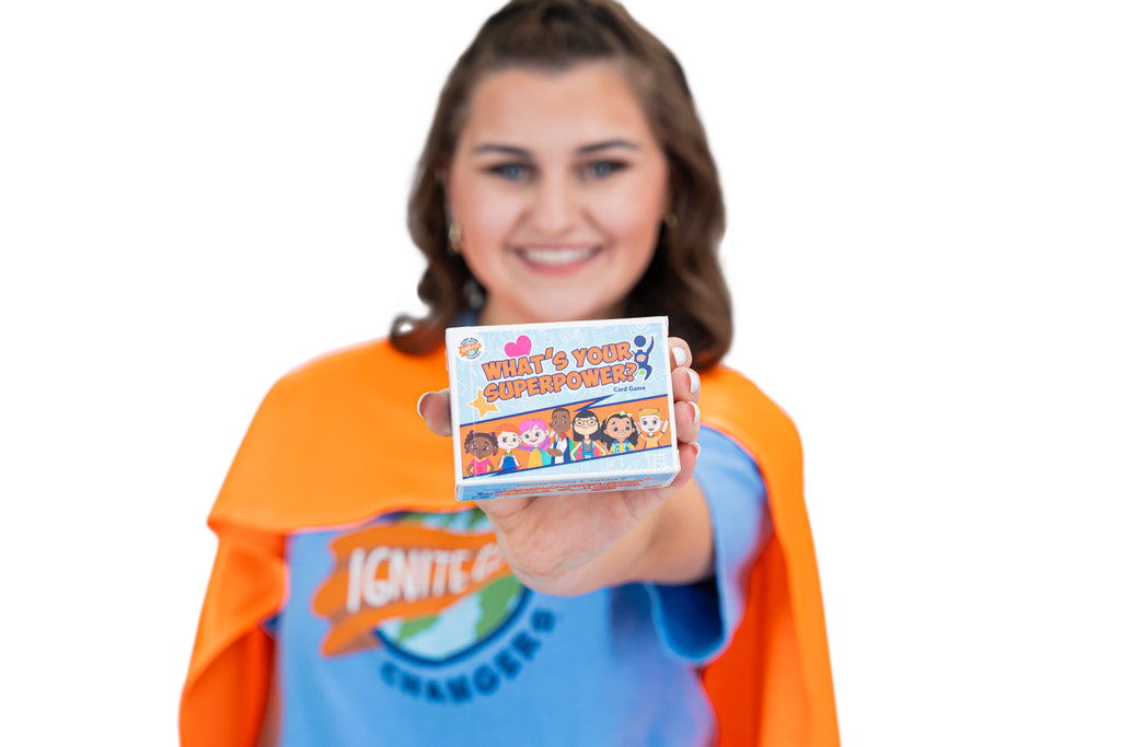 Women wearing an orange cape and blue superhero shirt holding the 'What's Your Superpower?' card game