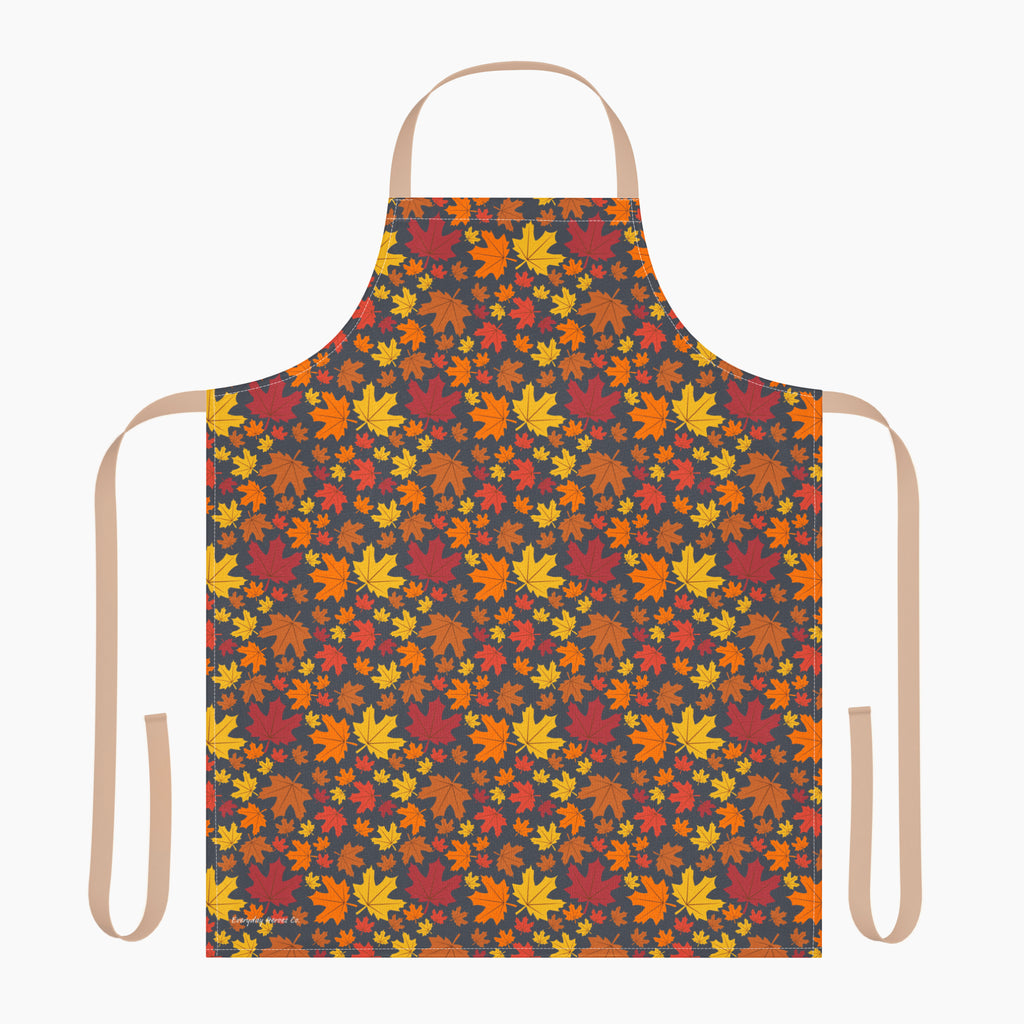 An apron with a colorful autumn leaf pattern, featuring a dark charcoal background with red, orange, yellow, and brown maple leaves. It has light beige neck and waist straps and is staged on a plain light-grey background.