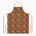An apron with a colorful autumn leaf pattern, featuring a dark charcoal background with red, orange, yellow, and brown maple leaves. It has light beige neck and waist straps and is staged on a plain light-grey background.