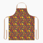 An apron with a colorful autumn leaf pattern, featuring a dark charcoal background with red, orange, yellow, and brown maple leaves. It has light beige neck and waist straps and is staged on a plain light-grey background.