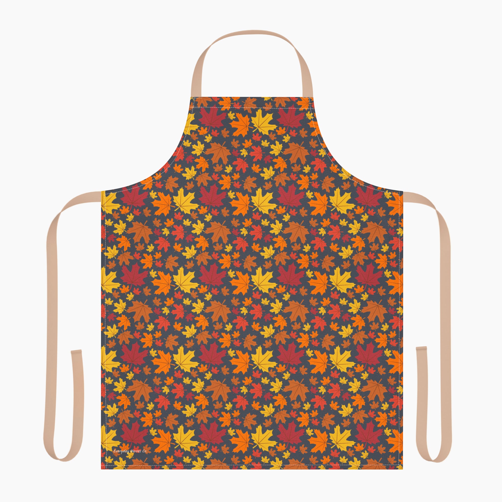 An apron with a colorful autumn leaf pattern, featuring a dark charcoal background with red, orange, yellow, and brown maple leaves. It has light beige neck and waist straps and is staged on a plain light-grey background.