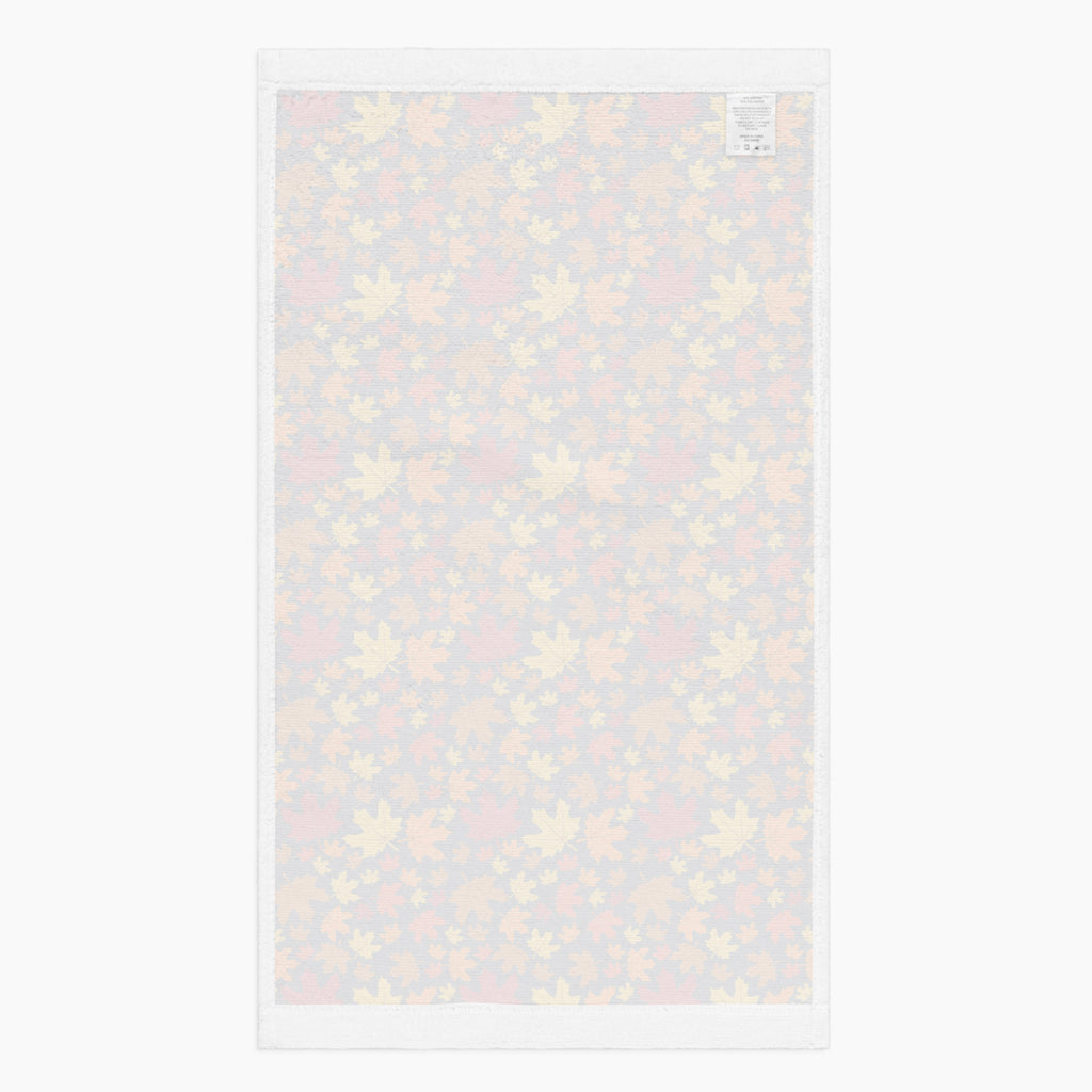 The white back side of a rectangular fabric kitchen towel featuring an all-over autumn maple leaf pattern in red, orange, yellow, and brown on a dark charcoal background, shown flat against a light gray backdrop.