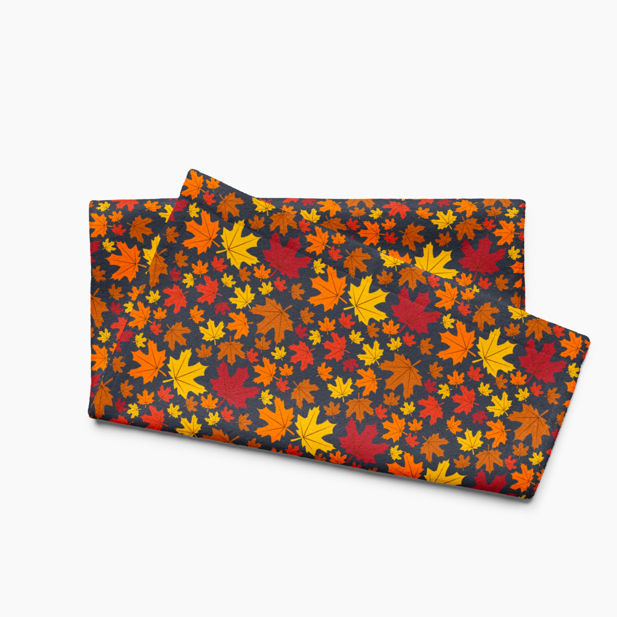A folded rectangular fabric kitchen towel featuring an all-over autumn maple leaf pattern in red, orange, yellow, and brown on a dark charcoal background, staged against a light gray backdrop.