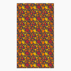 A rectangular fabric kitchen towel featuring an all-over autumn maple leaf pattern in red, orange, yellow, and brown on a dark charcoal background, shown flat against a light gray backdrop.