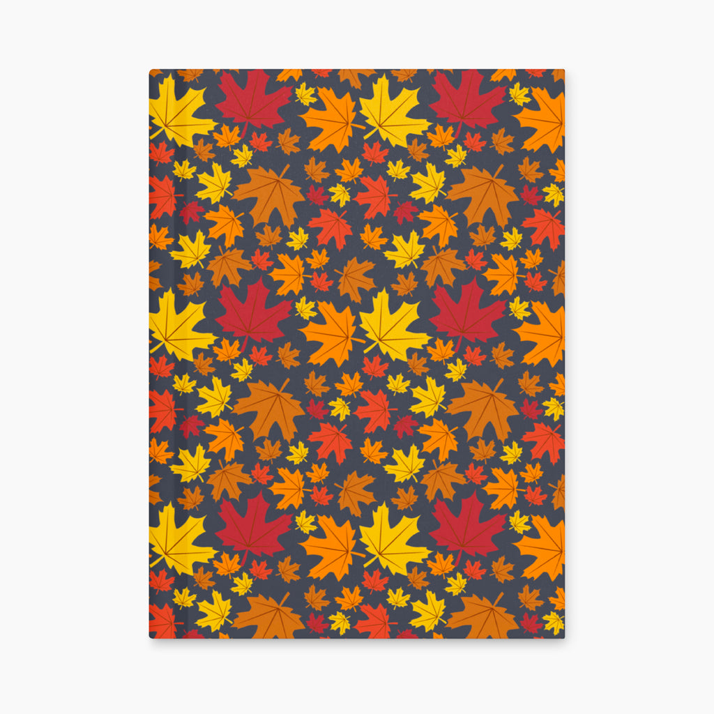 A notebook with a dark charcoal cover decorated with a dense pattern of colorful autumn maple leaves in red, orange, yellow, and brown, laying closed and flat against a light gray background.