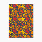 A notebook with a dark charcoal cover decorated with a dense pattern of colorful autumn maple leaves in red, orange, yellow, and brown, laying closed and flat against a light gray background.