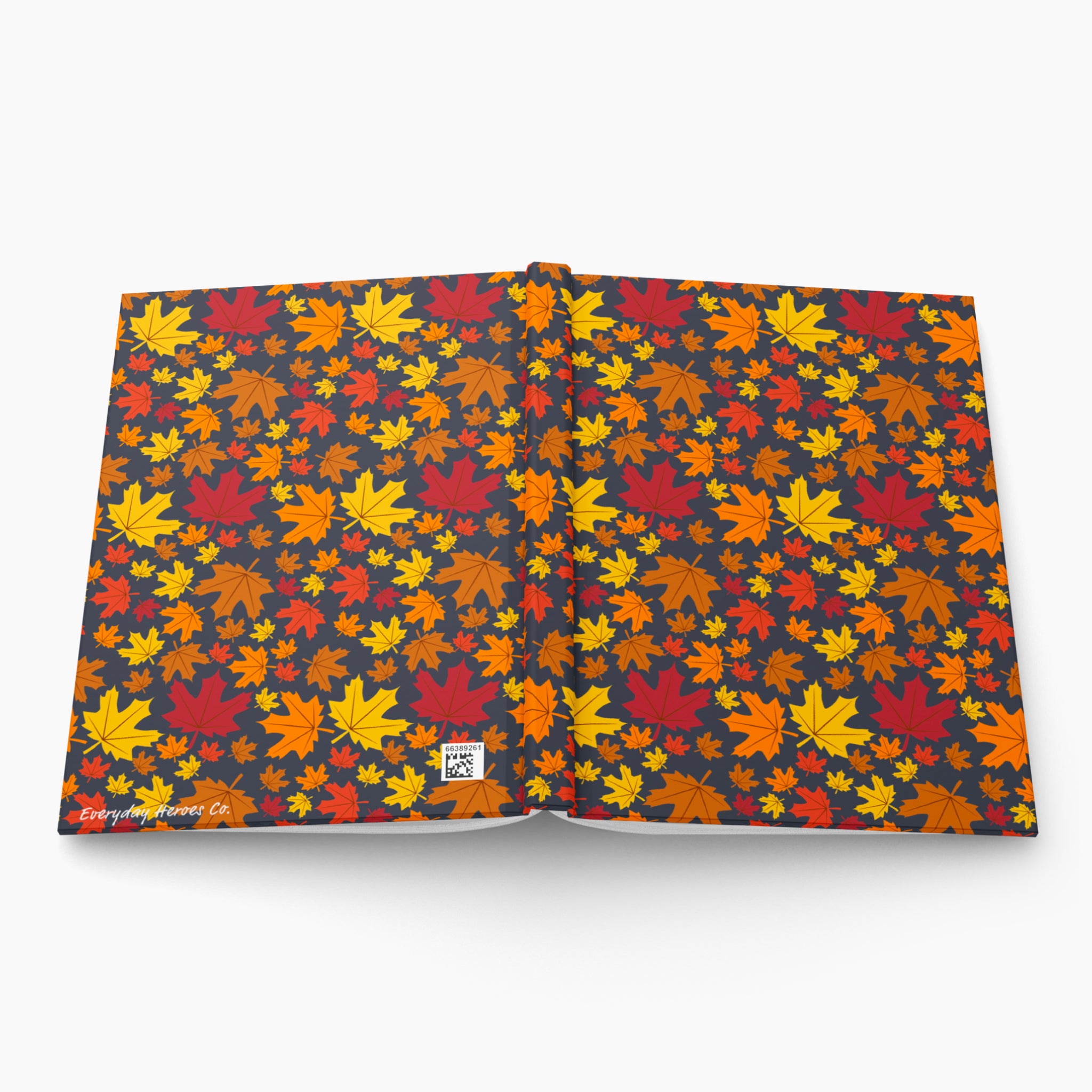 An open hardcover journal with a dark charcoal cover patterned all over with colorful autumn leaves in red, orange, yellow, and brown. A small white label is visible near the lower center, and the word 'Everyday Heroes Co' appears in script along the bottom left edge.