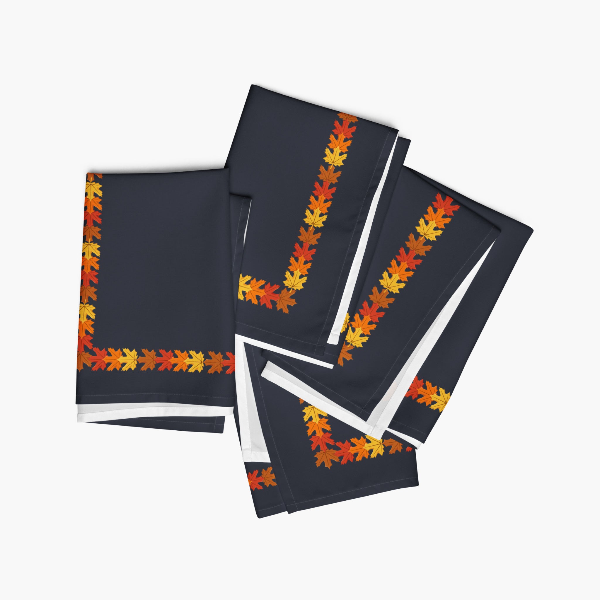 Four folded dark navy cloth napkins with a colorful autumn leaf border pattern in orange, yellow, and red, arranged on a light gray background.