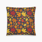 A square throw pillow featuring a dense pattern of colorful autumn maple leaves in shades of red, orange, yellow, and brown on a dark charcoal gray background, shown against a plain light grey studio backdrop.