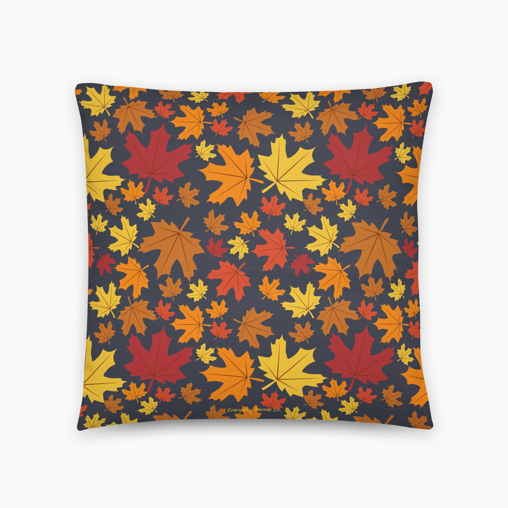 A square throw pillow featuring a dense pattern of colorful autumn maple leaves in shades of red, orange, yellow, and brown on a dark charcoal gray background, shown against a plain light grey studio backdrop.