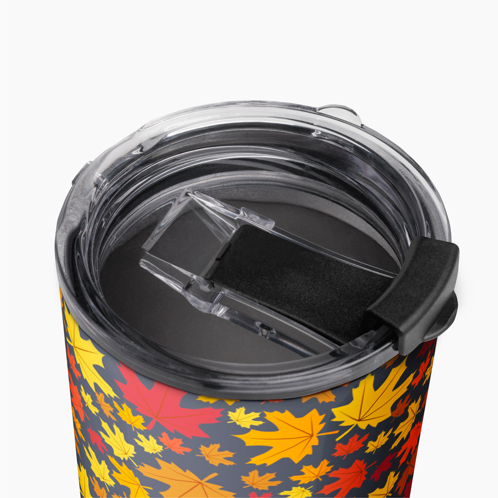 Close-up of a travel tumbler with a clear lid and black flip cover, featuring an all-over autumn leaf pattern in yellow, orange, and red on a dark background.