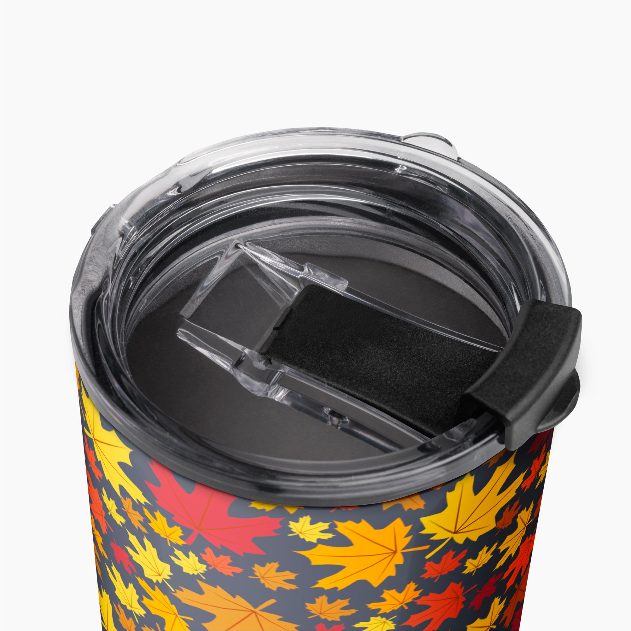 Close-up of a travel tumbler with a clear lid and black flip cover, featuring an all-over autumn leaf pattern in yellow, orange, and red on a dark background.