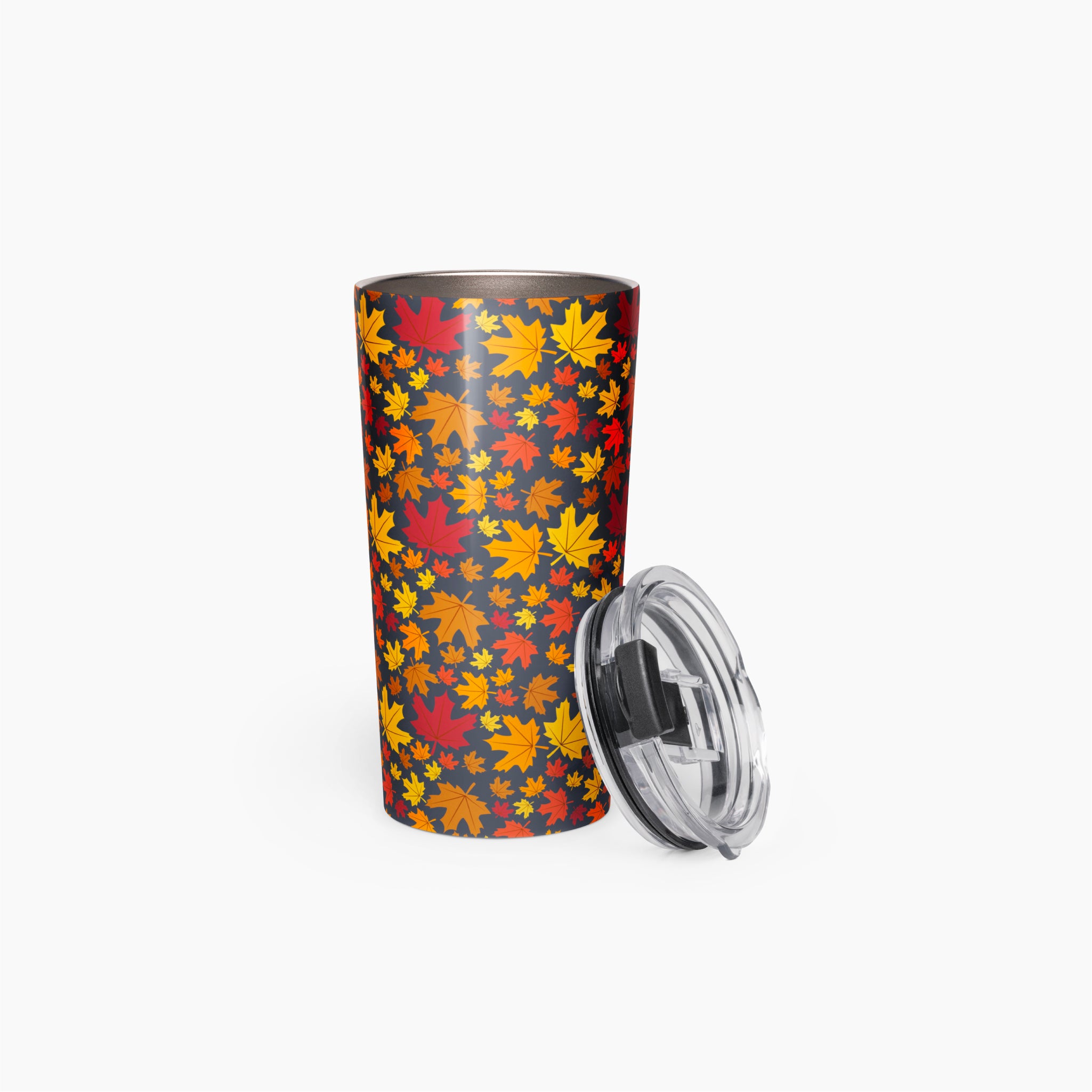 A tall insulated travel tumbler with a dark gray background covered in a dense pattern of red, orange, yellow, and yellow-orange autumn leaves. A clear plastic lid with a black rim is shown leaning against the right side of the tumbler staged on a clean light-grey background.
