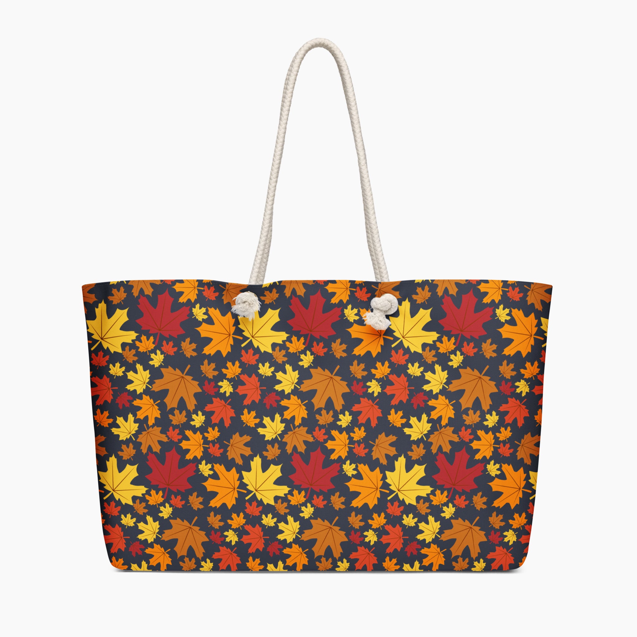 A tote bag with a dense autumn maple leaf pattern in red, orange, yellow, and brown on a dark charcoal background, featuring  white handles.