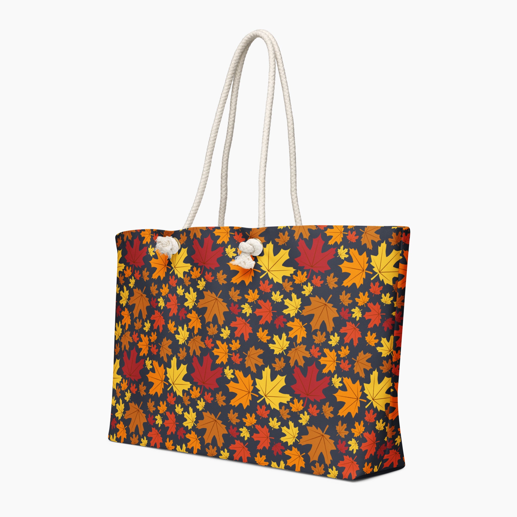 A tote bag with a dense autumn maple leaf pattern in red, orange, yellow, and brown on a dark charcoal background, featuring  white handles.
