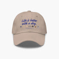 Beige cap with 'Life is better with a dog' text and dog icons on a white background