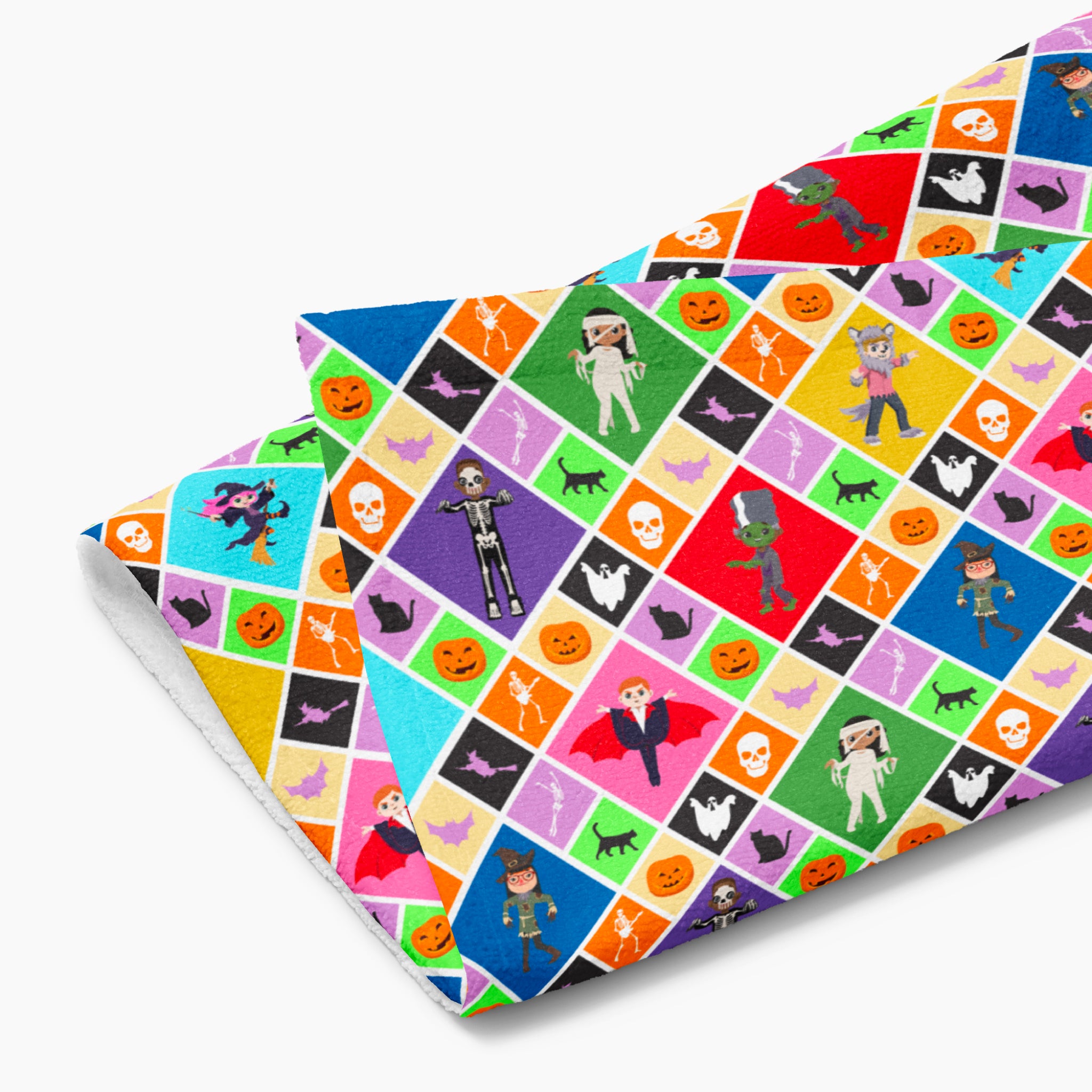 A folded kitchen towel featuring a Halloween-themed diamond pattern with pumpkins, ghosts, bats, a skeleton, and cartoon kids in costumes, shown on a light gray background.