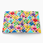 An open hardcover notebook or journal displaying a vibrant, repeating Halloween-themed pattern on its pages. The pattern consists of colorful diamond tiles featuring illustrations of witches, ghosts, skeletons, pumpkins, cats, and cartoon kids costumes, shown on a light grey background.