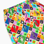 A closeup of a pair of colorful pajama pants with an all-over geometric pattern of repeating diamonds in multiple bright colors, featuring halloween themed pumpkins, skulls, batts, cats, witches, ghosts, and cartoon kids in costumes shown flat against a light gray background.