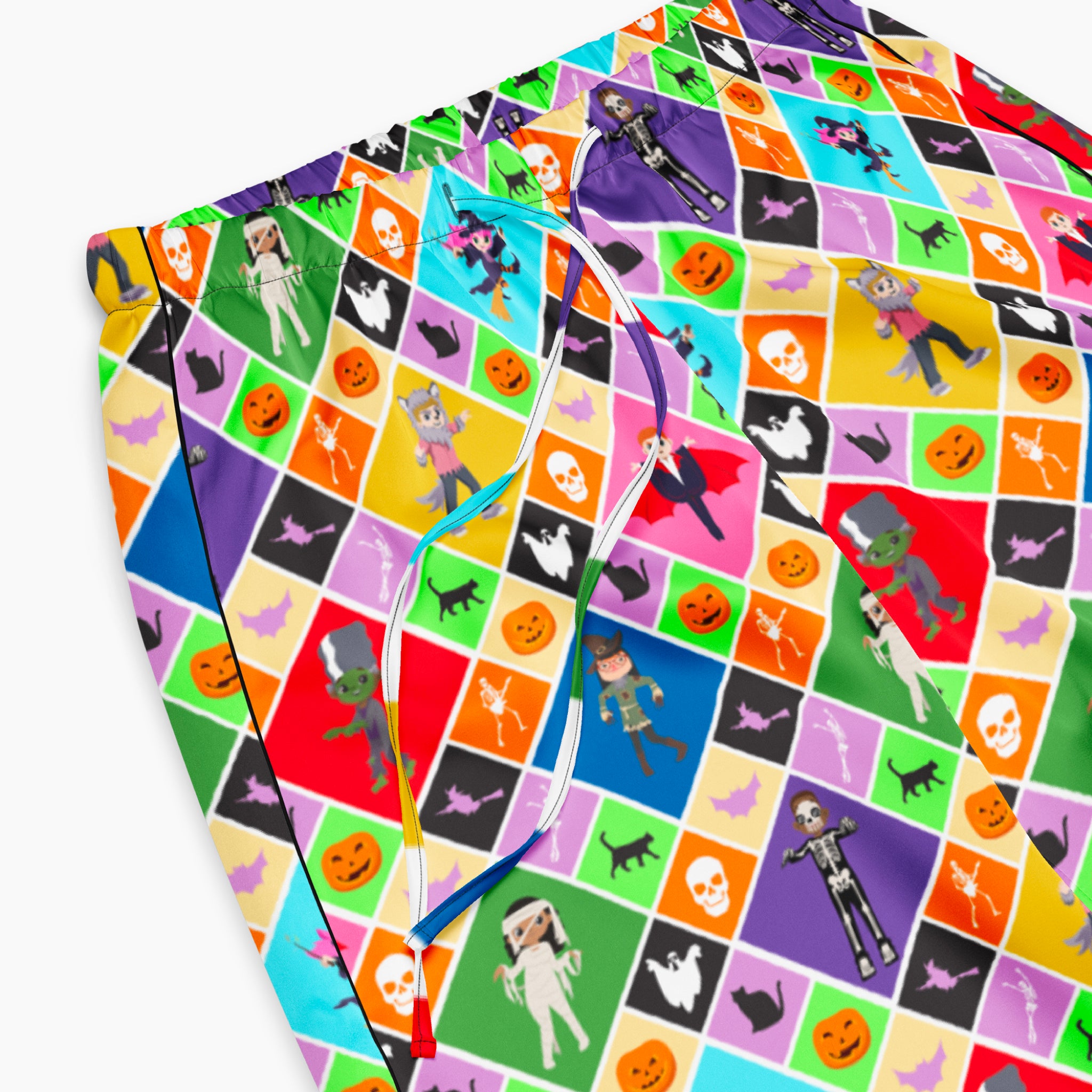 A closeup of a pair of colorful pajama pants with an all-over geometric pattern of repeating diamonds in multiple bright colors, featuring halloween themed pumpkins, skulls, batts, cats, witches, ghosts, and cartoon kids in costumes shown flat against a light gray background.