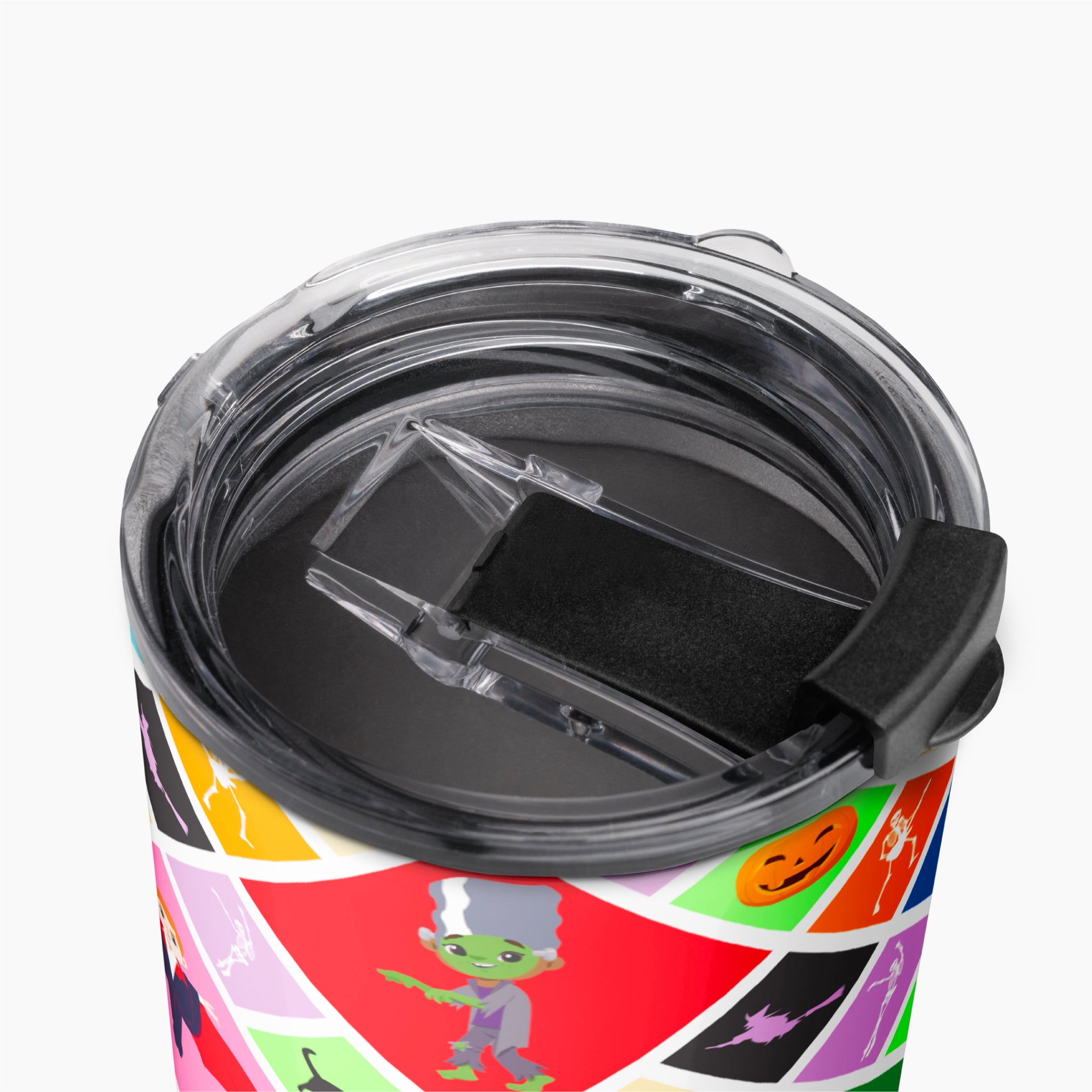 Close-up of a travel tumbler with a clear lid and black flip cover, featuring a colorful geometric print with Halloween motifs on a light grey background.