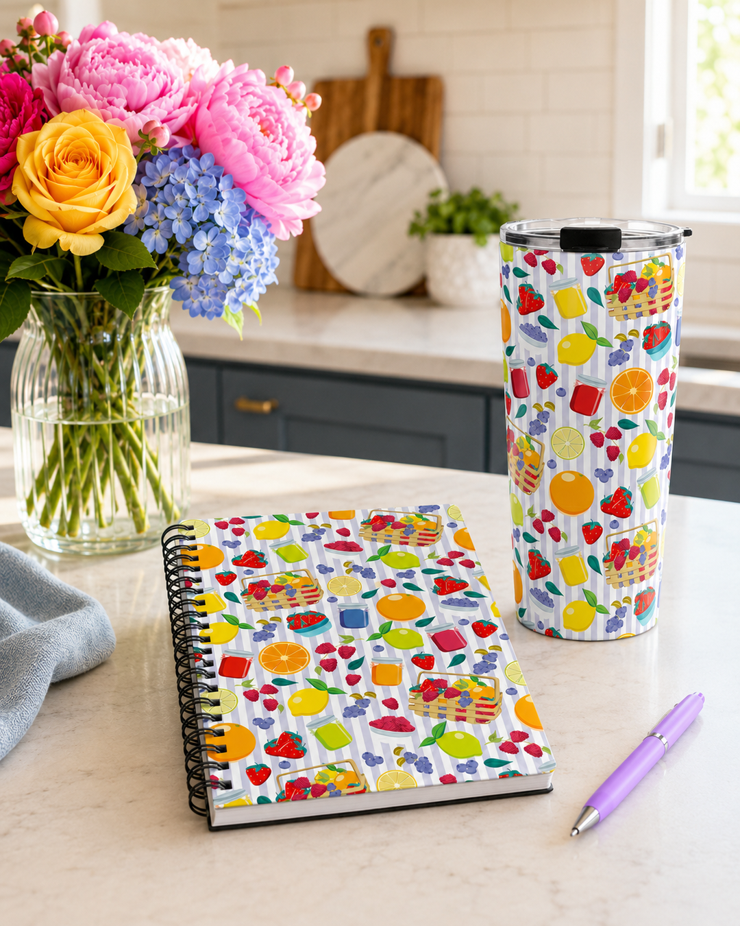Custom printed notebook and tumbler with a Summer Fruit pattern on a table with flowers and pen.