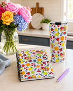 Custom printed Summer Fruit themed notebook and tumbler on a table with flowers and pen.