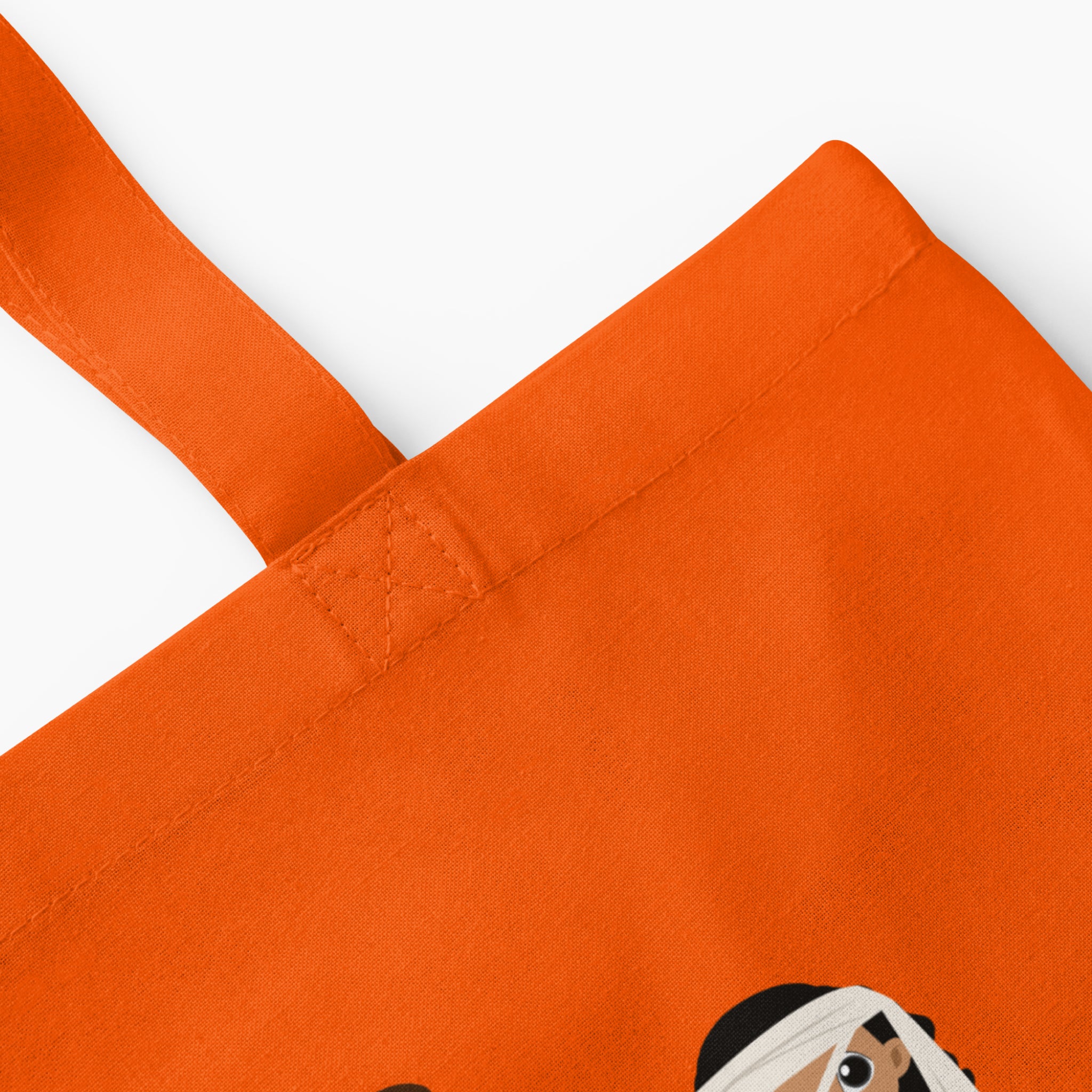 Close-up of an orange canvas tote bag with a partial cartoon graphic visible at the bottom right corner, set against a clean light grey background.