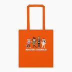 An orange canvas tote bag with orange handles, featuring a graphic of four cartoon monsters and the text 'MONSTERS ASSEMBLE!' printed on the front, set against a plain light grey background.