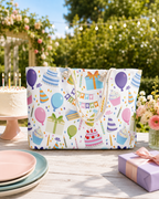 Colorful tote bag with birthday-themed design on a table outdoors with cake and flowers.