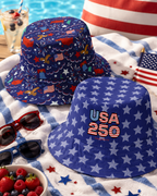 Two blue bucket hats with custom patriotic designs by a pool on a towel with berries and sunglasses.