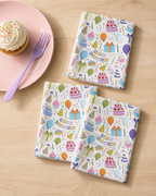 Three colorful napkins with custom printed birthday-themed patterns on a wooden surface with a cupcake and purple fork.