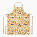 A white apron with a beige neck loop and waist ties, featuring an all-over autumn pattern of pumpkins, sunflowers, gourds, and fall leaves.