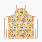 A white apron with a beige neck loop and waist ties, featuring an all-over autumn pattern of pumpkins, sunflowers, gourds, and fall leaves.