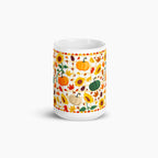 A white ceramic mug featuring a colorful autumn-themed pattern with pumpkins, sunflowers, maple leaves, and acorns, shown on a light gray background.