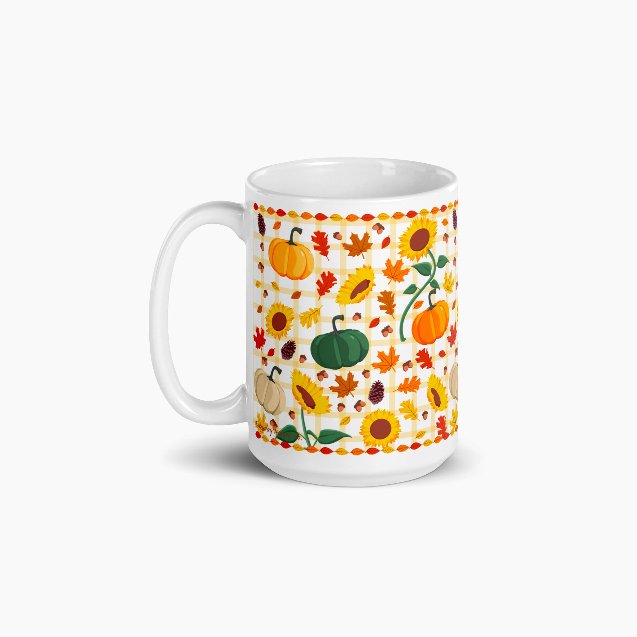 A white ceramic mug decorated with a colorful autumn pattern featuring pumpkins, sunflowers, maple leaves, and acorns on a light gray background.
