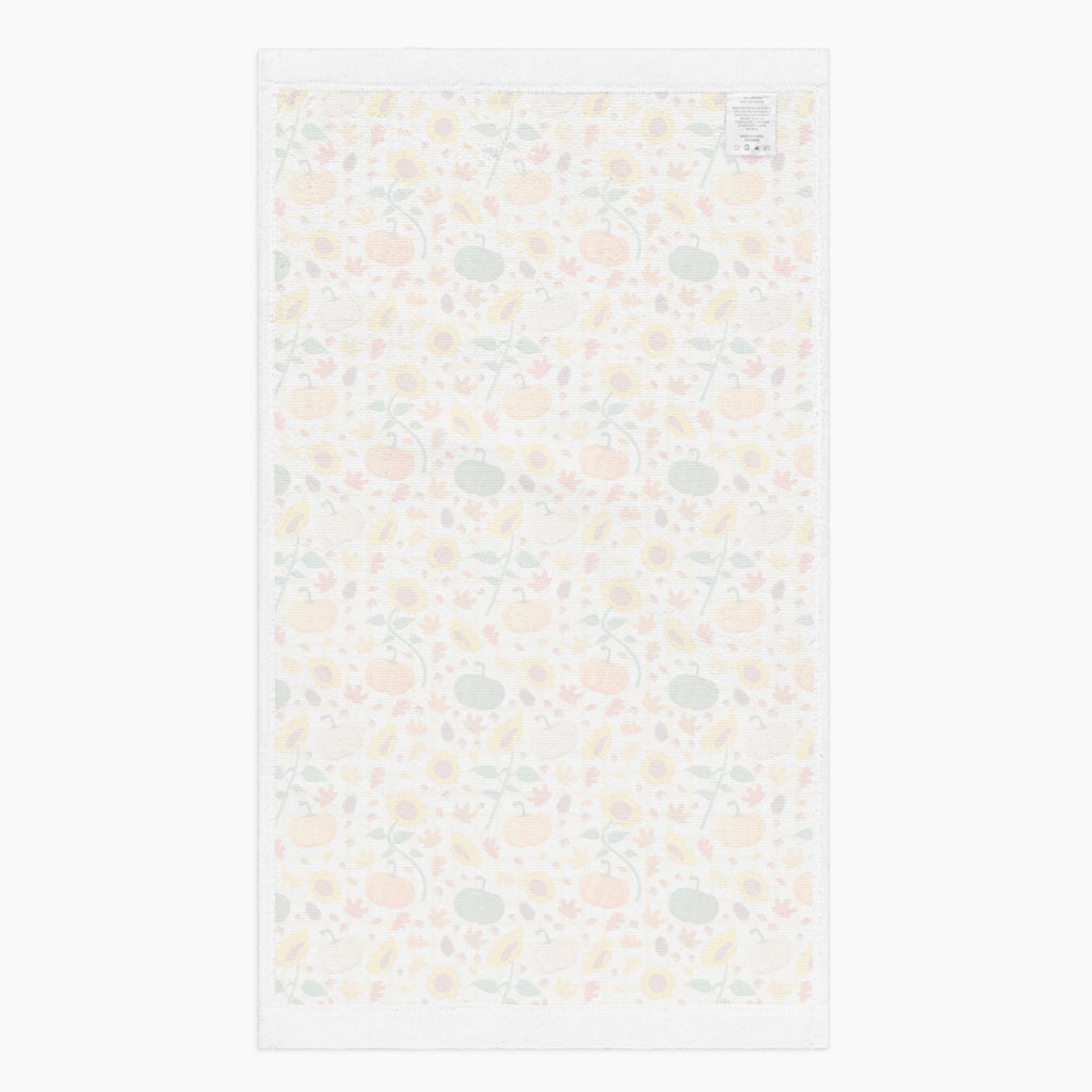 The white backside of rectangular dish towel featuring all-over autumnal leaf, pumpkin, and sunflower pattern, shown flat against a light gray background.