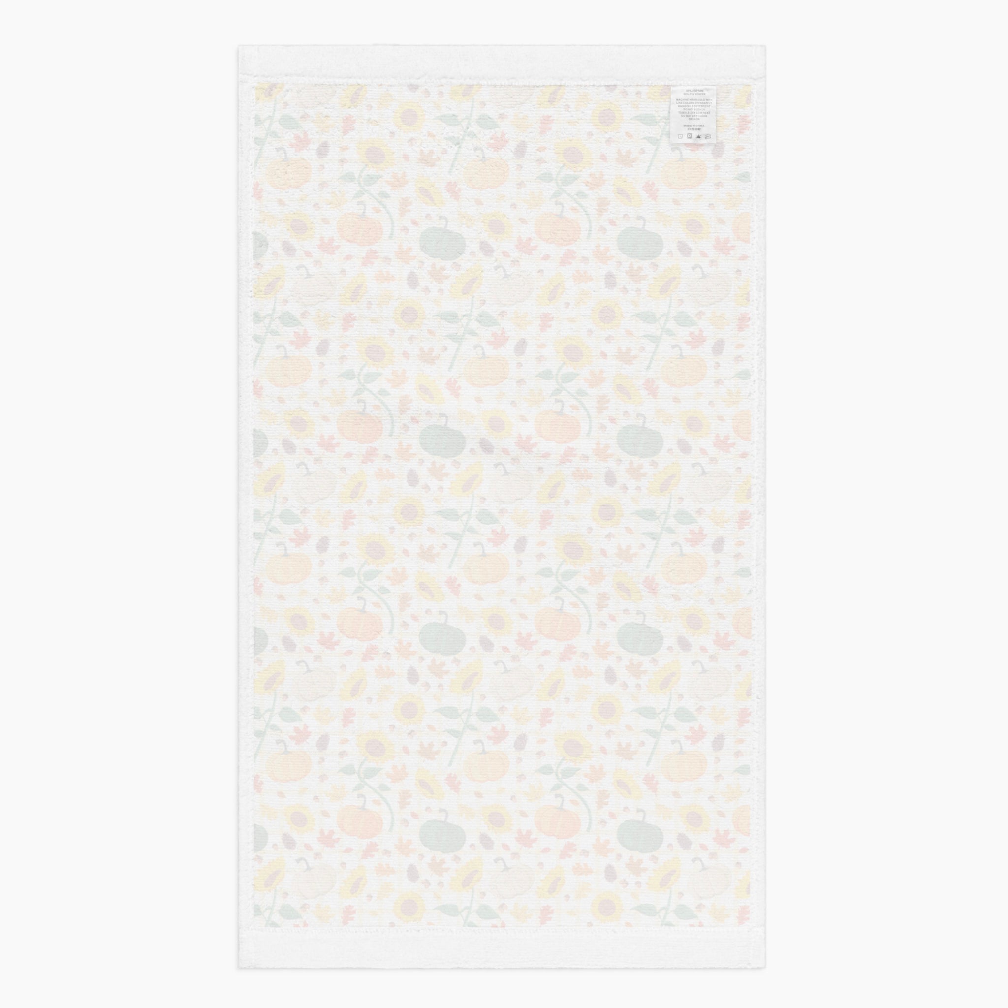 The white backside of rectangular dish towel featuring all-over autumnal leaf, pumpkin, and sunflower pattern, shown flat against a light gray background.