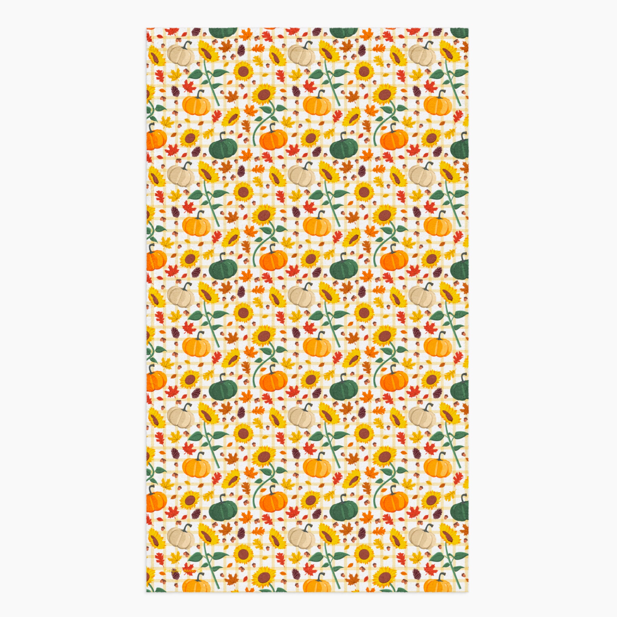 A dish towel featuring a repeating autumn pattern of pumpkins, sunflowers, gourds, acorns, and leaves on a light-grey studio backdrop.
