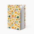 A hardcover notebook with a white cover decorated with a colorful autumn pattern of pumpkins, sunflowers, and leaves, standing upright on a light gray background.