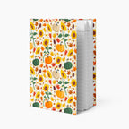 A hardcover notebook with a white cover decorated with a colorful autumn pattern of pumpkins, sunflowers, and leaves, standing upright on a light gray background.