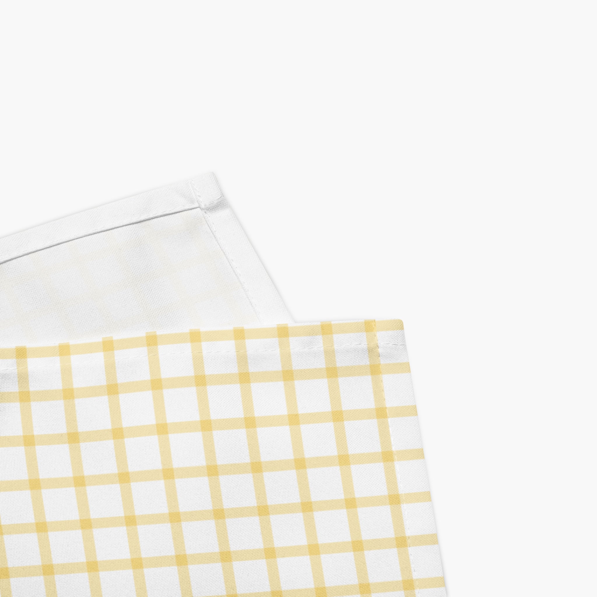 A close-up of a white cloth napkin folded to show a yellow gingham check pattern on one side and a plain white reverse side on the other, set against a light grey studio background.