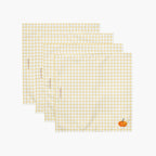 Four square white napkins with a yellow gingham check pattern, arranged in a staggered stack. Each napkin features a small pumpkin in the bottom right corner, and the napkins have subtle red text saying "Everyday Heroes Co" printed vertically along the left side.