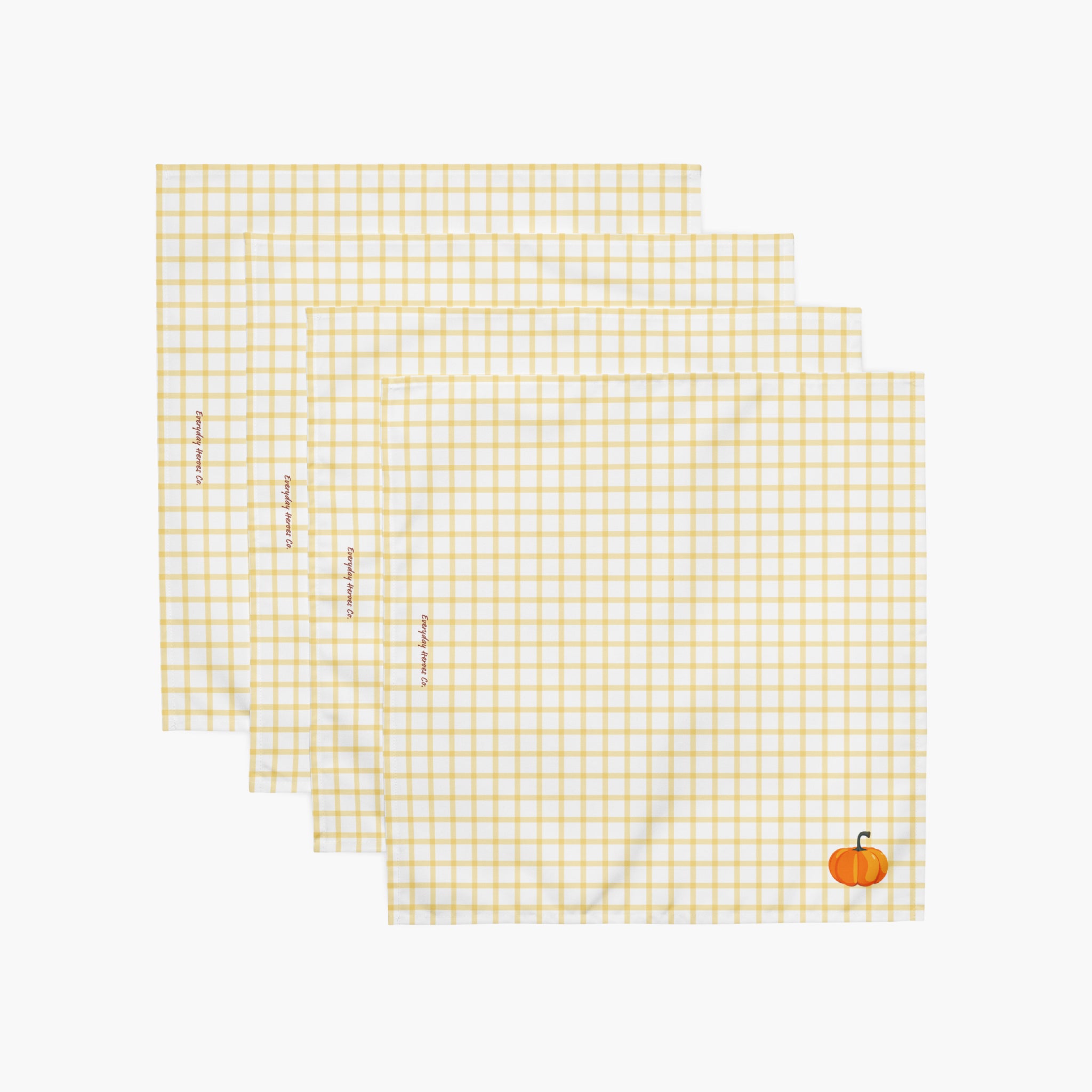 Four square white napkins with a yellow gingham check pattern, arranged in a staggered stack. Each napkin features a small pumpkin in the bottom right corner, and the napkins have subtle red text saying "Everyday Heroes Co" printed vertically along the left side.