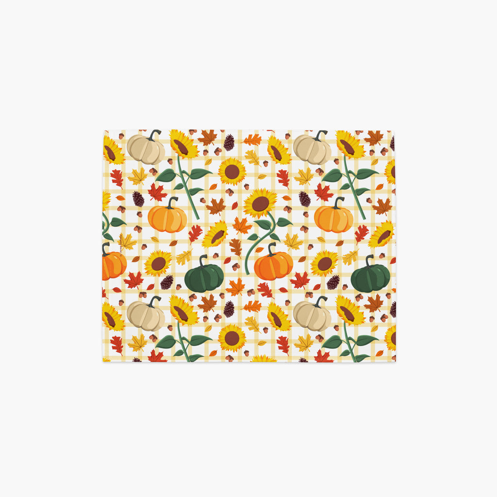 A rectangular placemat, featuring a repeating autumn pattern of pumpkins, sunflowers, maple leaves, and pinecones on a light-grey studio background.