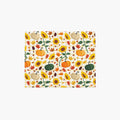 A rectangular placemat, featuring a repeating autumn pattern of pumpkins, sunflowers, maple leaves, and pinecones on a light-grey studio background.