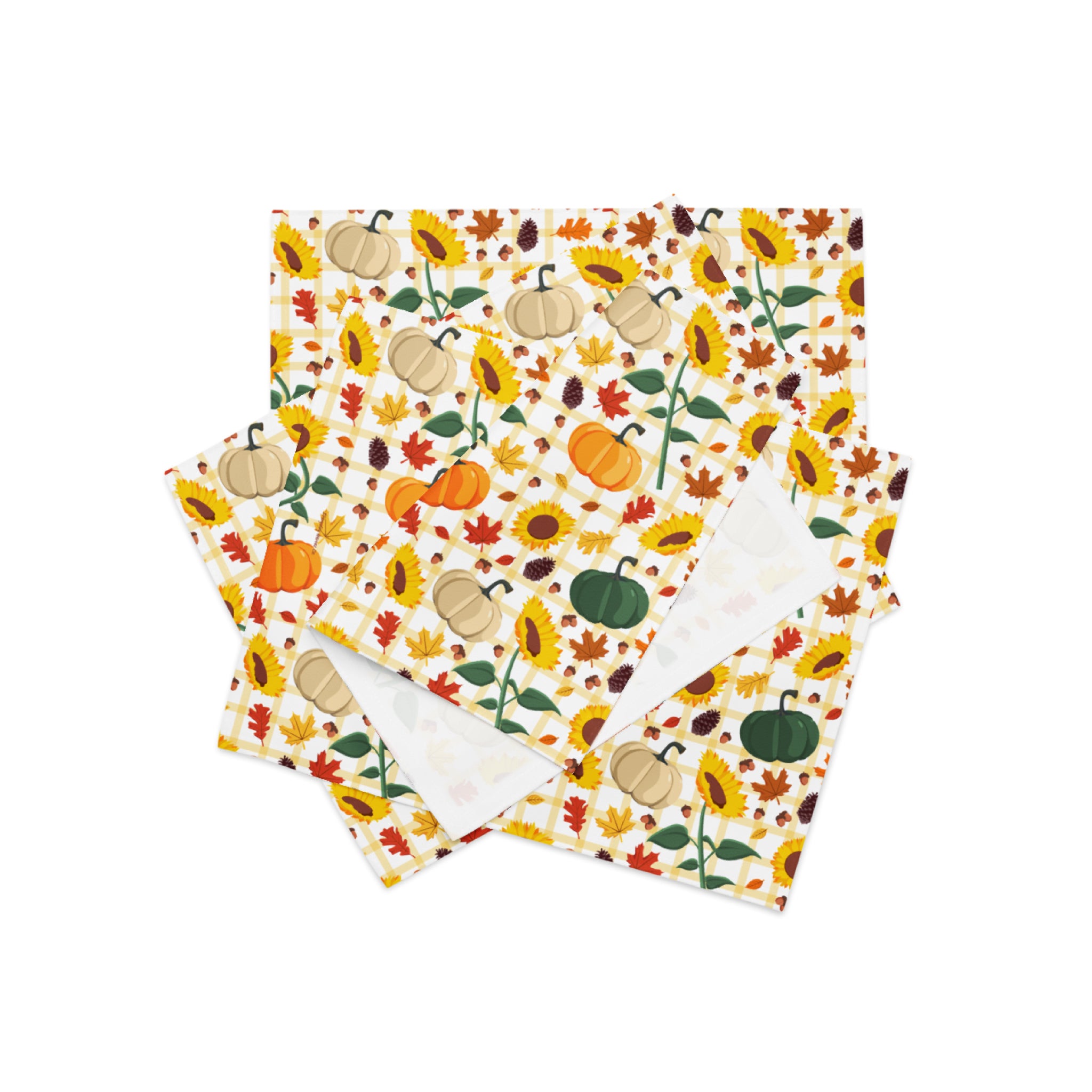 A stack of cloth placemats featuring a colorful autumn pattern with pumpkins, sunflowers, leaves, and acorns on a cream background, with one napkin showing a plain white reverse side.