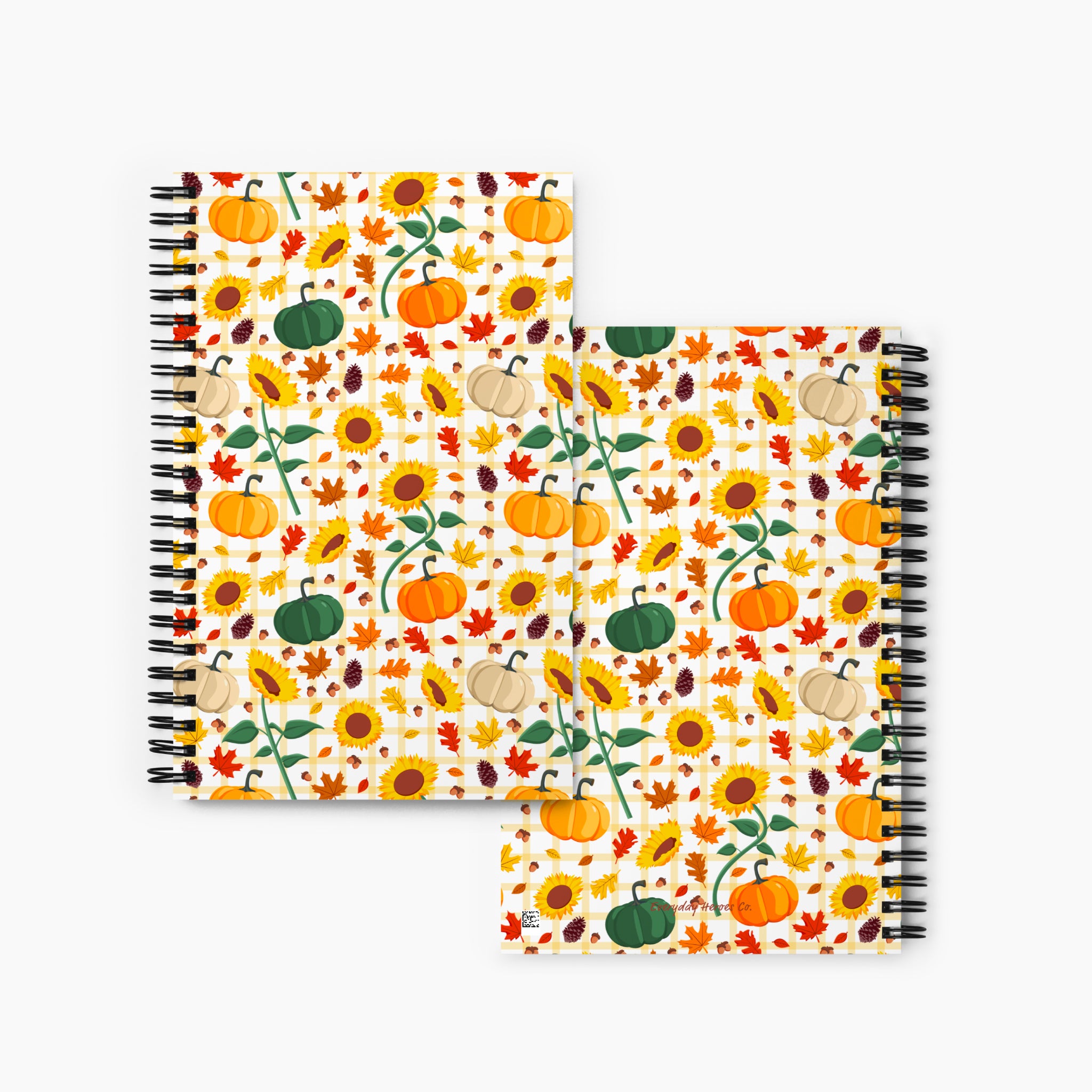 Front and back covers of a spiral-bound notebook with a colorful autumn pattern featuring pumpkins, sunflowers, maple leaves, and acorns on a cream background, displayed against a light gray studio backdrop.
