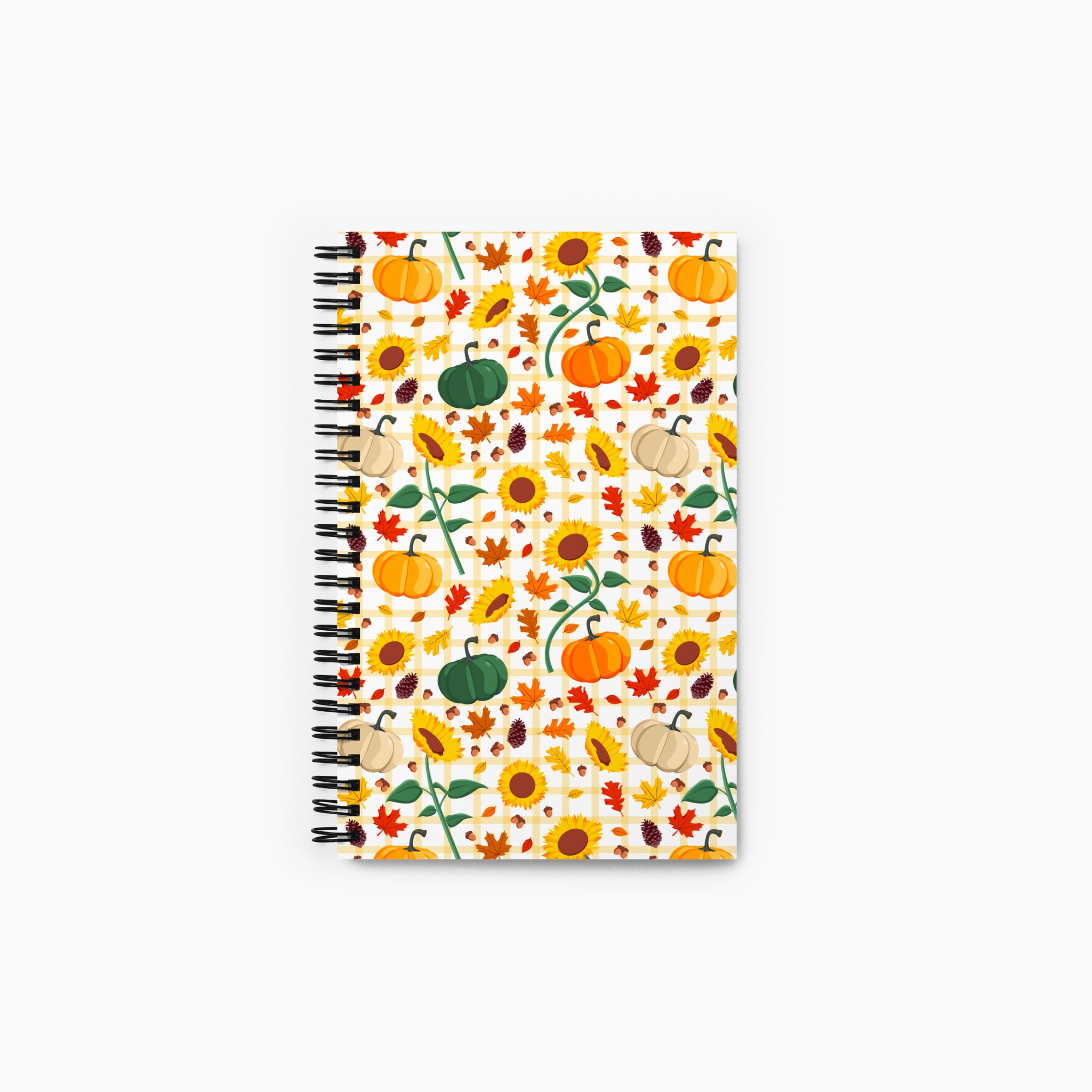 A spiral-bound notebook with a white cover decorated with an autumn pattern of pumpkins, sunflowers, maple leaves, pinecones, and acorns, shown against a plain light-grey background.