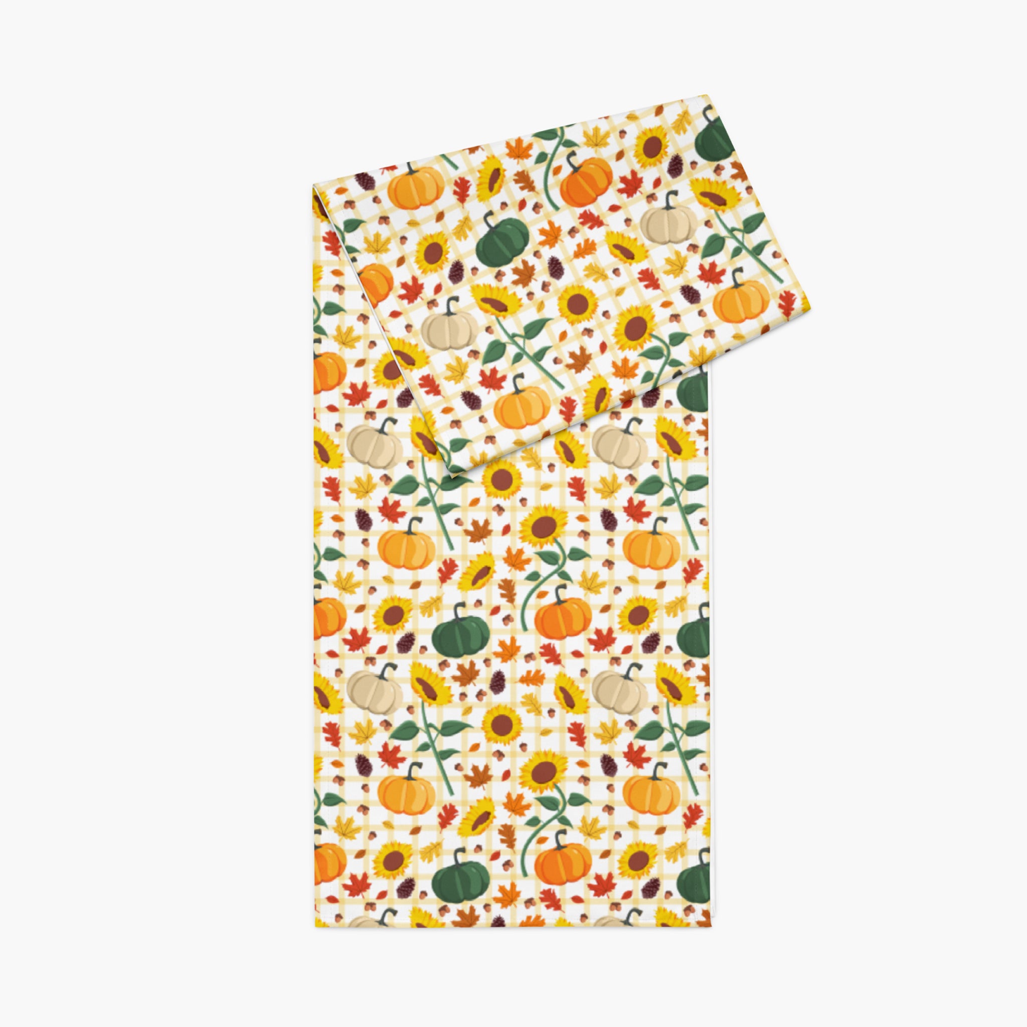 A folded table runner featuring a colorful autumn pattern of pumpkins, sunflowers, and maple leaves on a light-grey background.